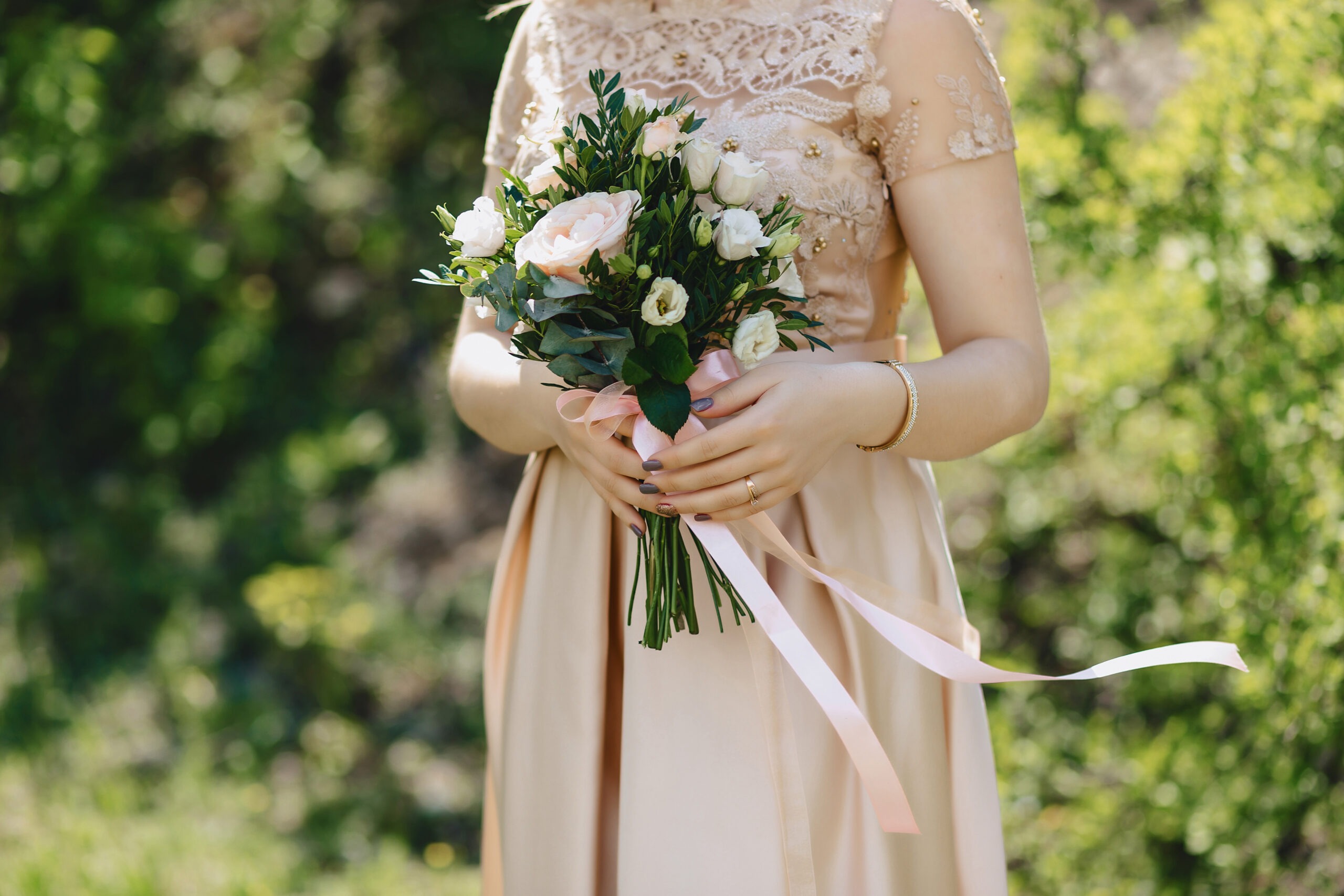 Brautjungfer in einem champagnerfarbenen Kleid hält einen Hochzeitsstrauß mit rosa und weißen Blumen.Brautjungfer in einem champagnerfarbenen Kleid hält einen Hochzeitsstrauß mit rosa und weißen Blumen.