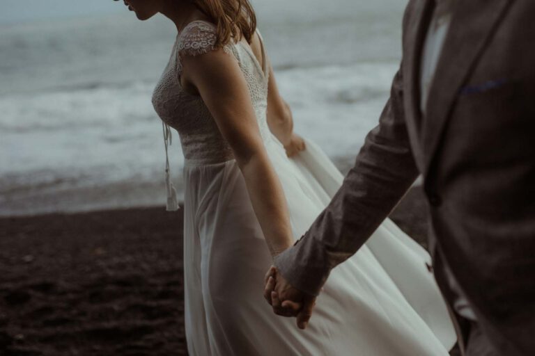 Braut und Bräutigam halten Händchen am Strand.